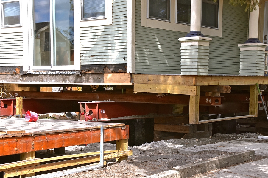 an old house rests on steel girders as a new concrete basement and foundation is being created